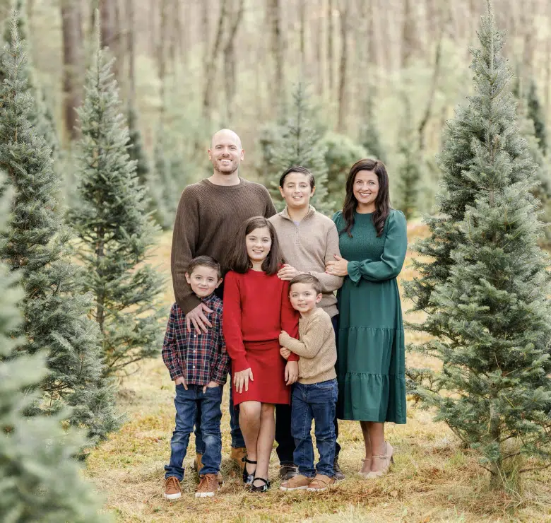 Photo of Jennifer with her husband and four children in a woodland setting among small fraser fir trees