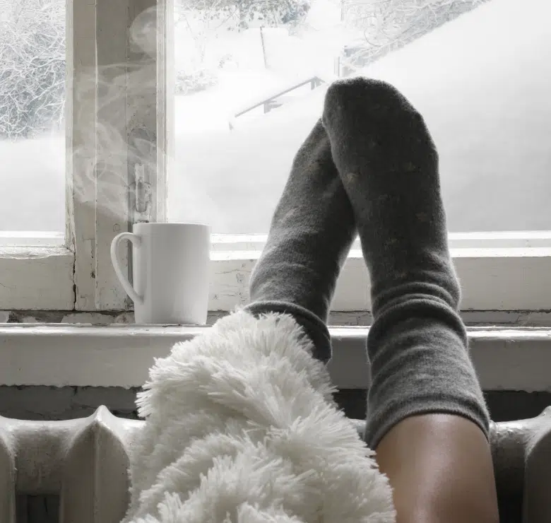 a woman's feet in warm socks propped on a windowsill with lots of snow outside the window